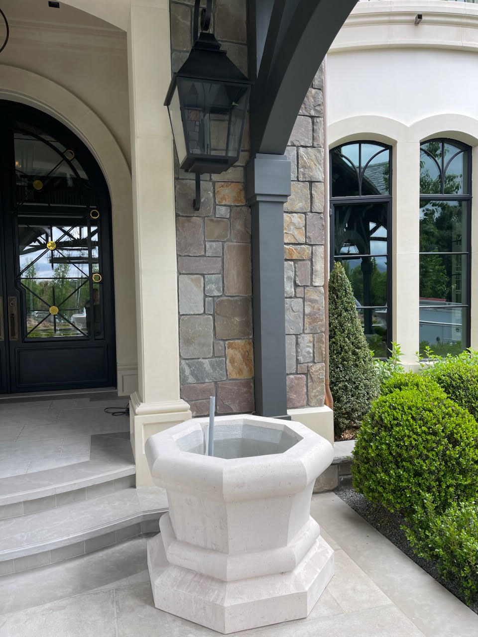 Octagonal cast stone entry fountain beside an arched front door